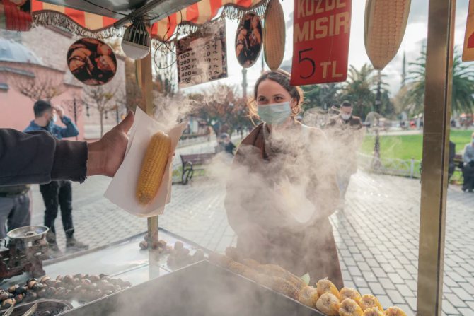 Девушка в маске покупает горячую кукурузу в Стамбуле